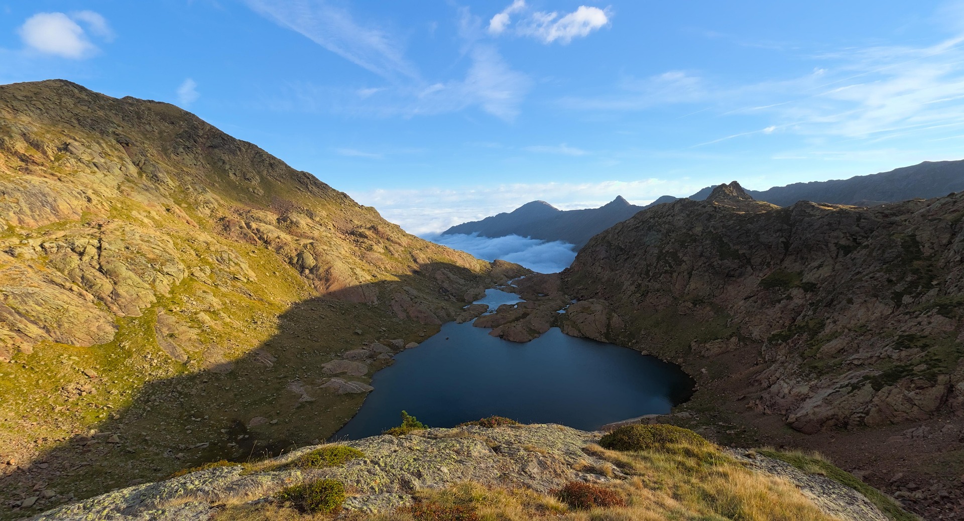 Vue en hauteur d’un lac de montagne dans les Pyrénées ariégeoises, nuages dans la vallée en contrebas